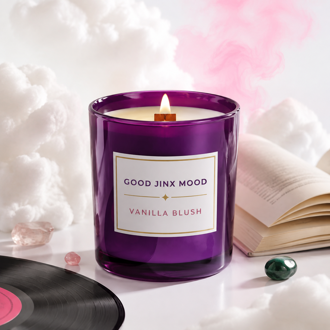 Good Jinx Mood Vanilla Blush candle beside an open book and vinyl record in a dreamlike cloud setting